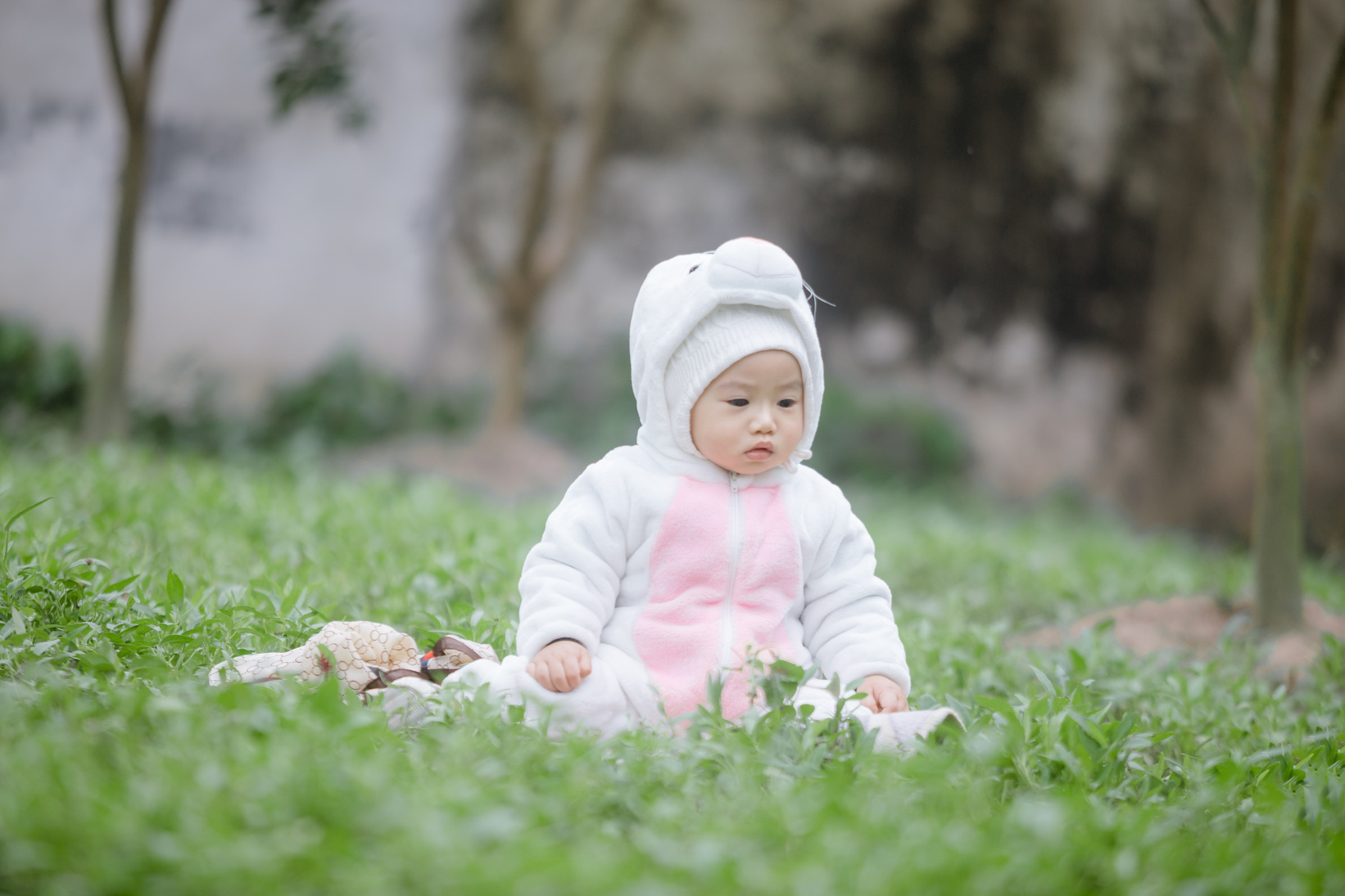 A Baby in White Hoodie Sitting on a Green Grass